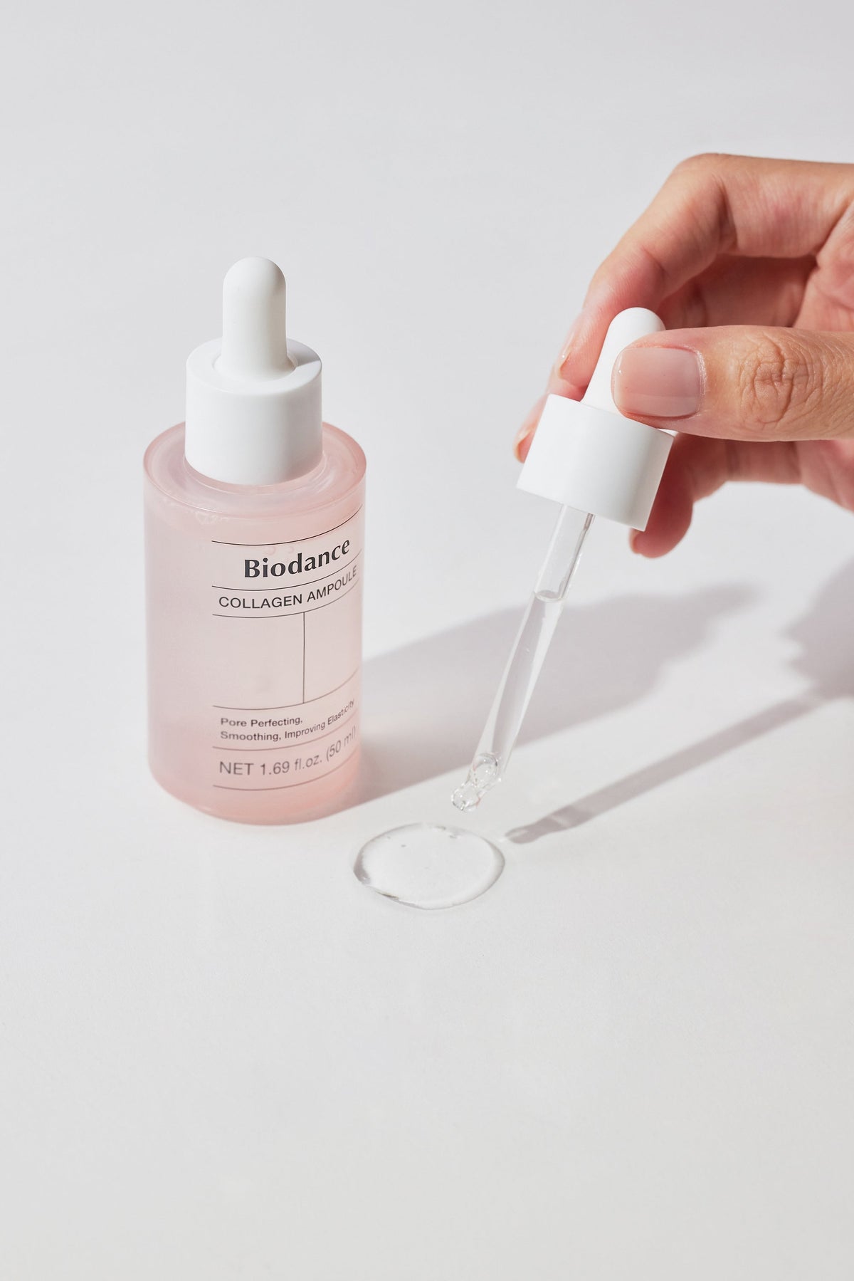 Ampoule transparente déposée avec une pipette près du flacon rose