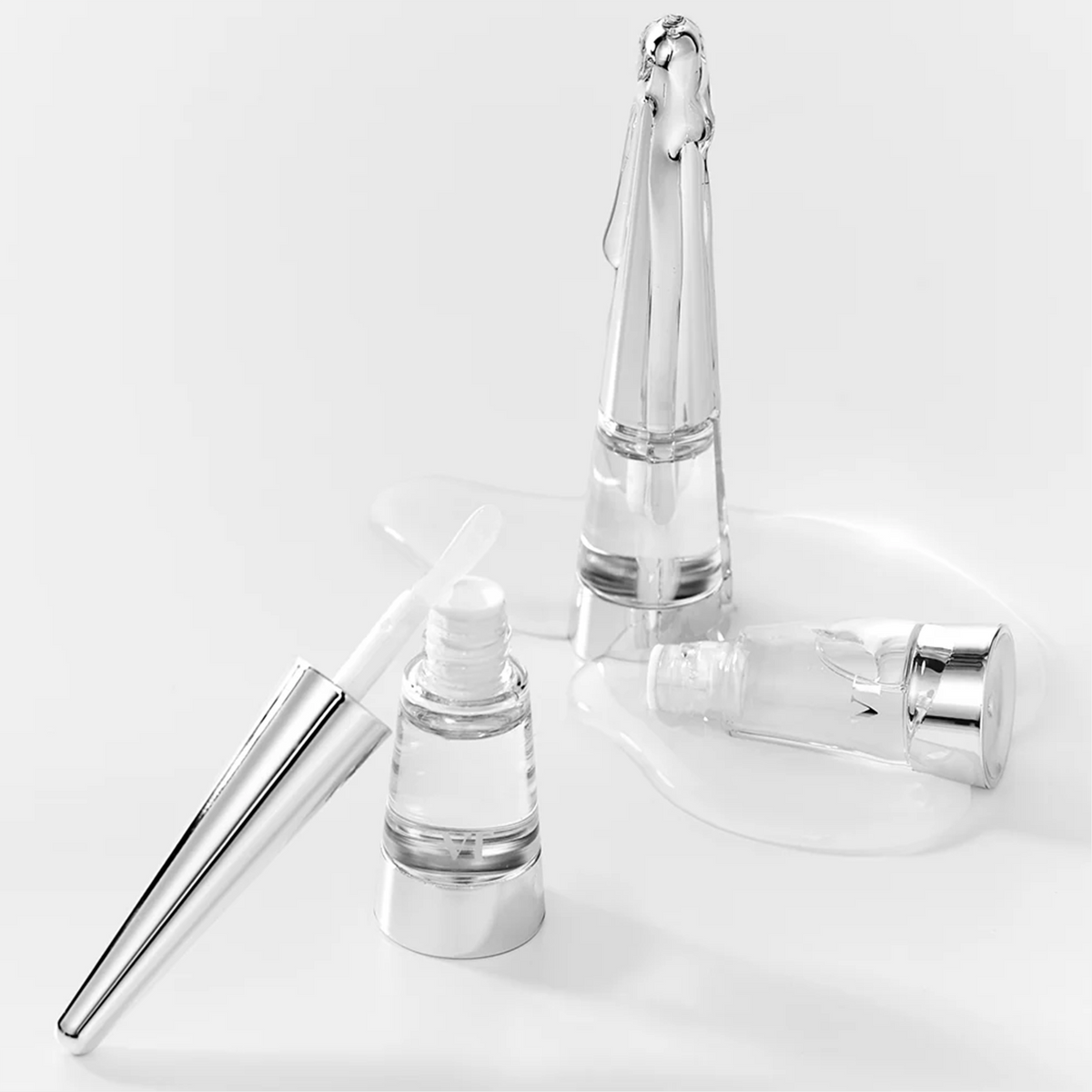 Flacons transparents de gloss et applicateur sur une flaque de gel