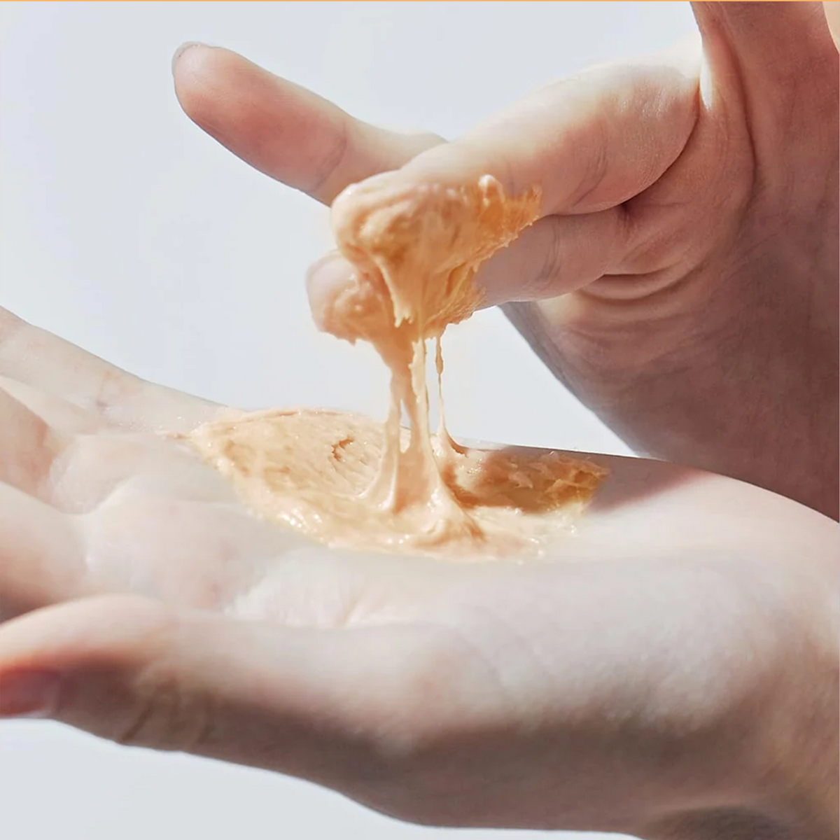 Pâte nettoyante beige étirée entre les doigts et la paume