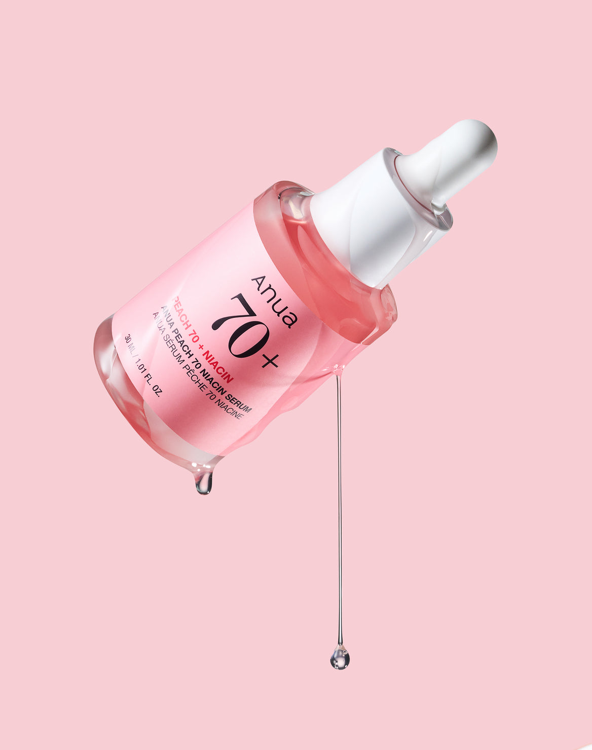 Flacon rose incliné avec des gouttes de sérum suspendues