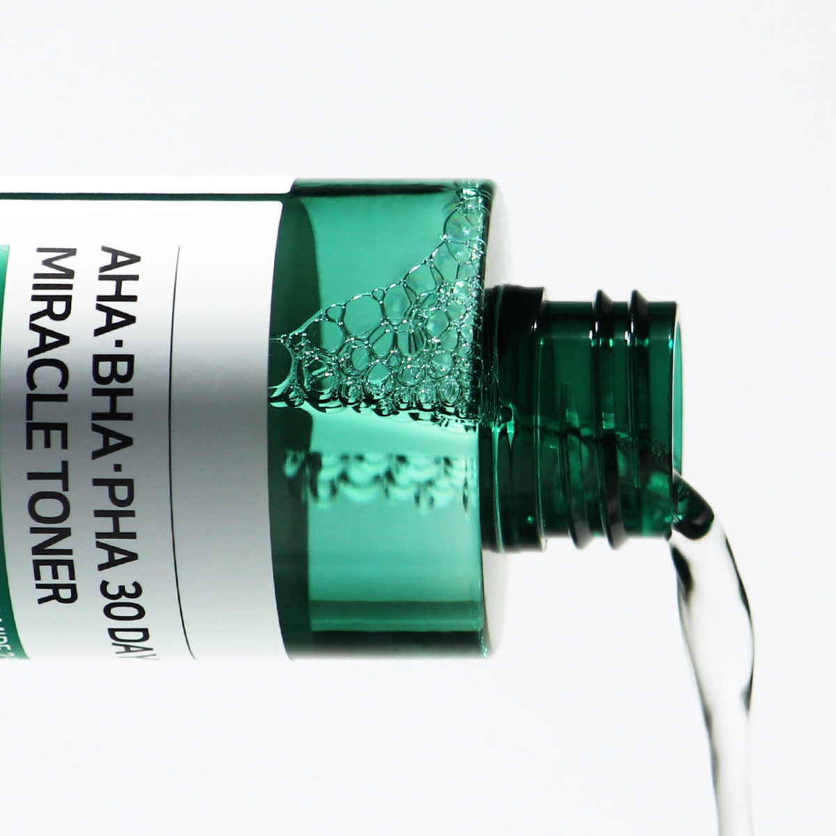 Lotion transparente versée depuis le flacon vert ouvert