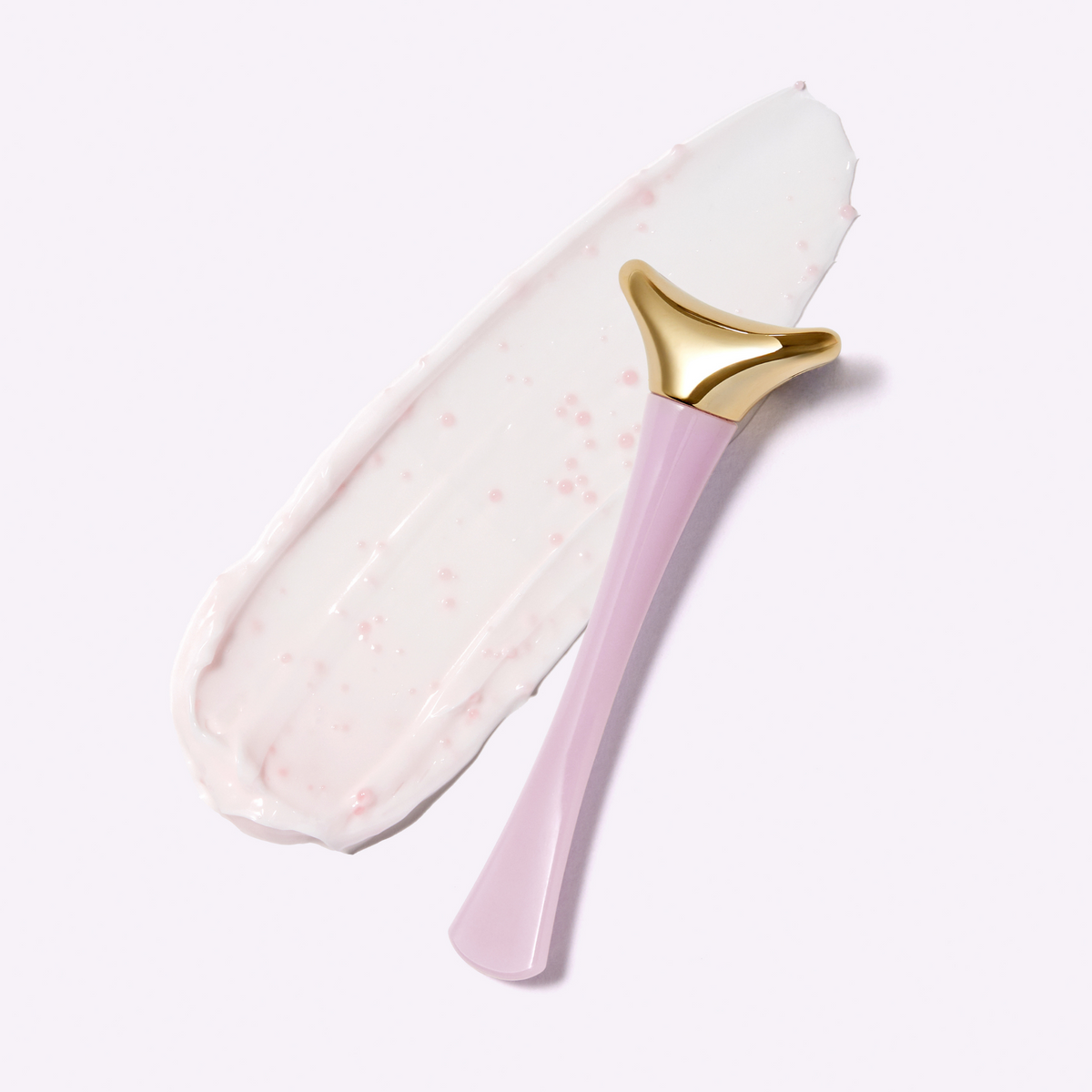 Applicateur à tête dorée posé sur une trace de crème rose pâle