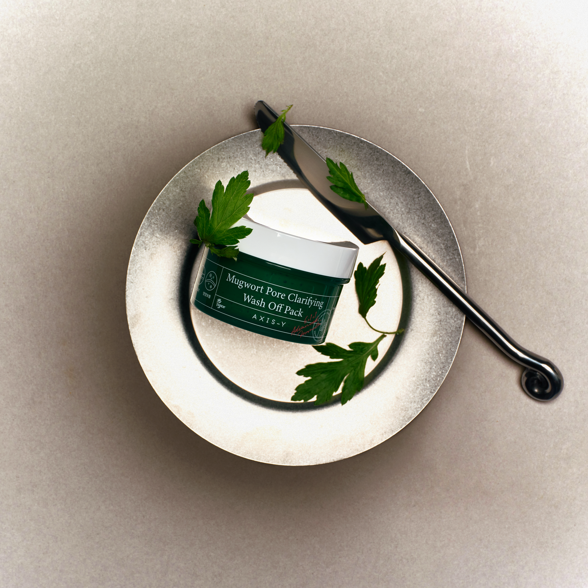 Pot de masque et spatule métallique sur une assiette avec des feuilles