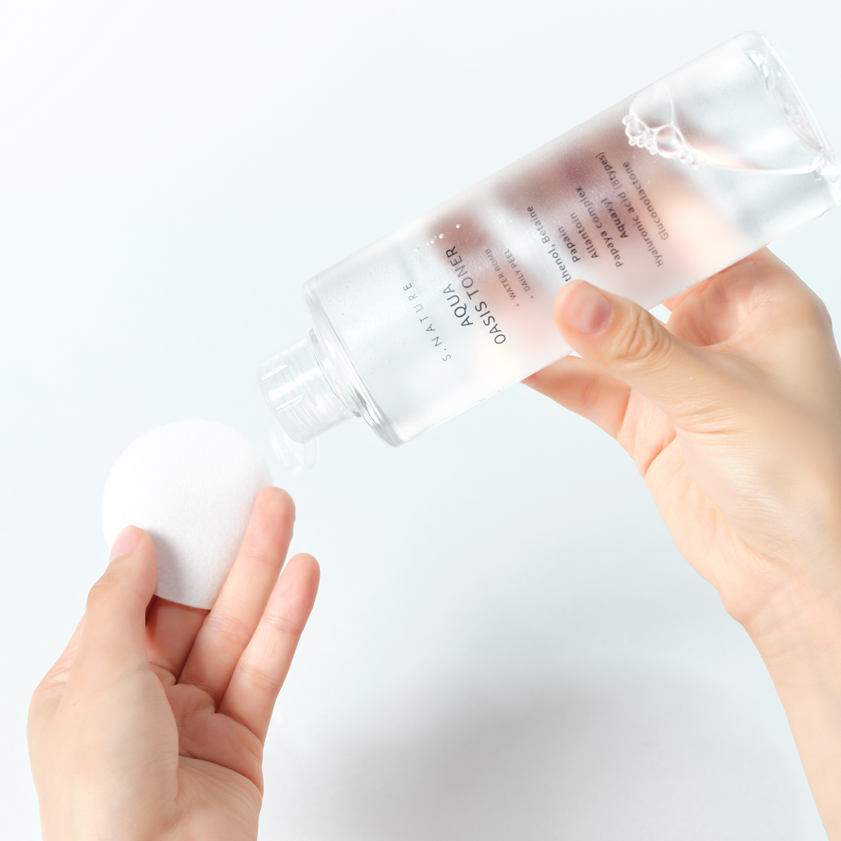 Lotion versée sur un coton rond tenu en main
