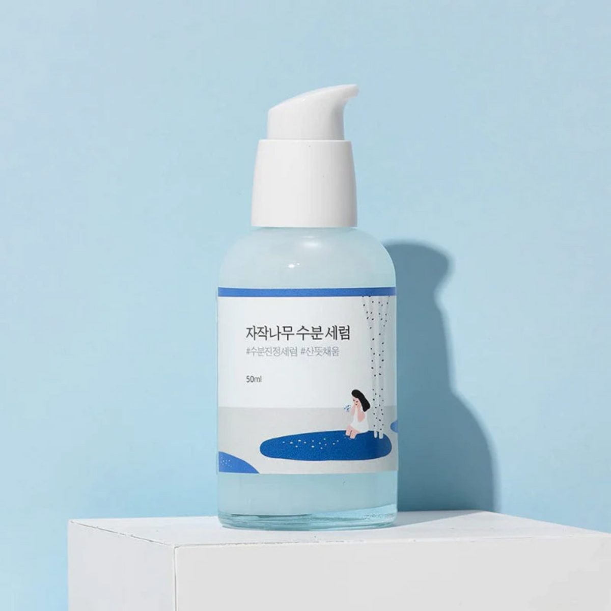 Flacon-pompe de sérum bleu clair posé sur un socle blanc