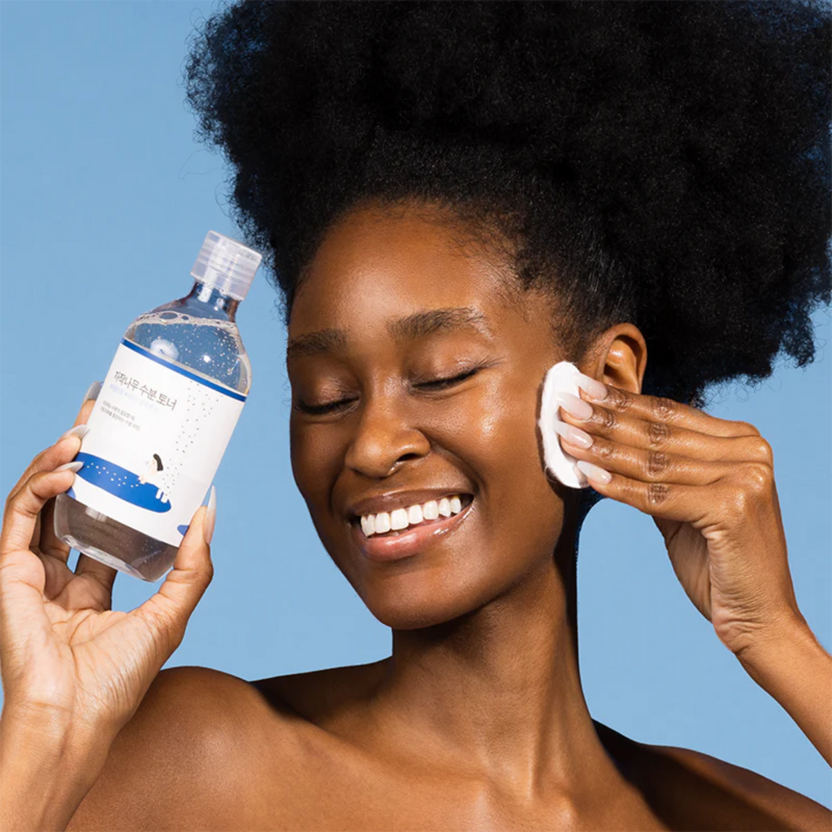 Lotion appliquée avec un coton sur la joue, flacon tenu dans l&