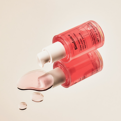 Flacon-pompe rose couché près de gouttes de sérum rose