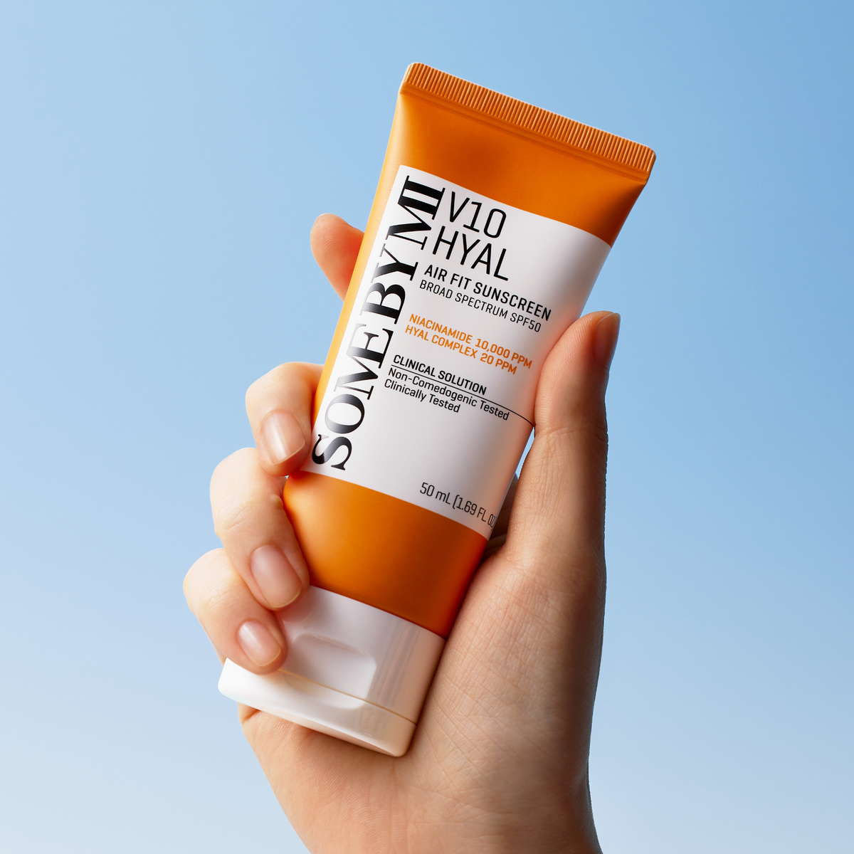 Tube orange et blanc de crème solaire tenu dans la main
