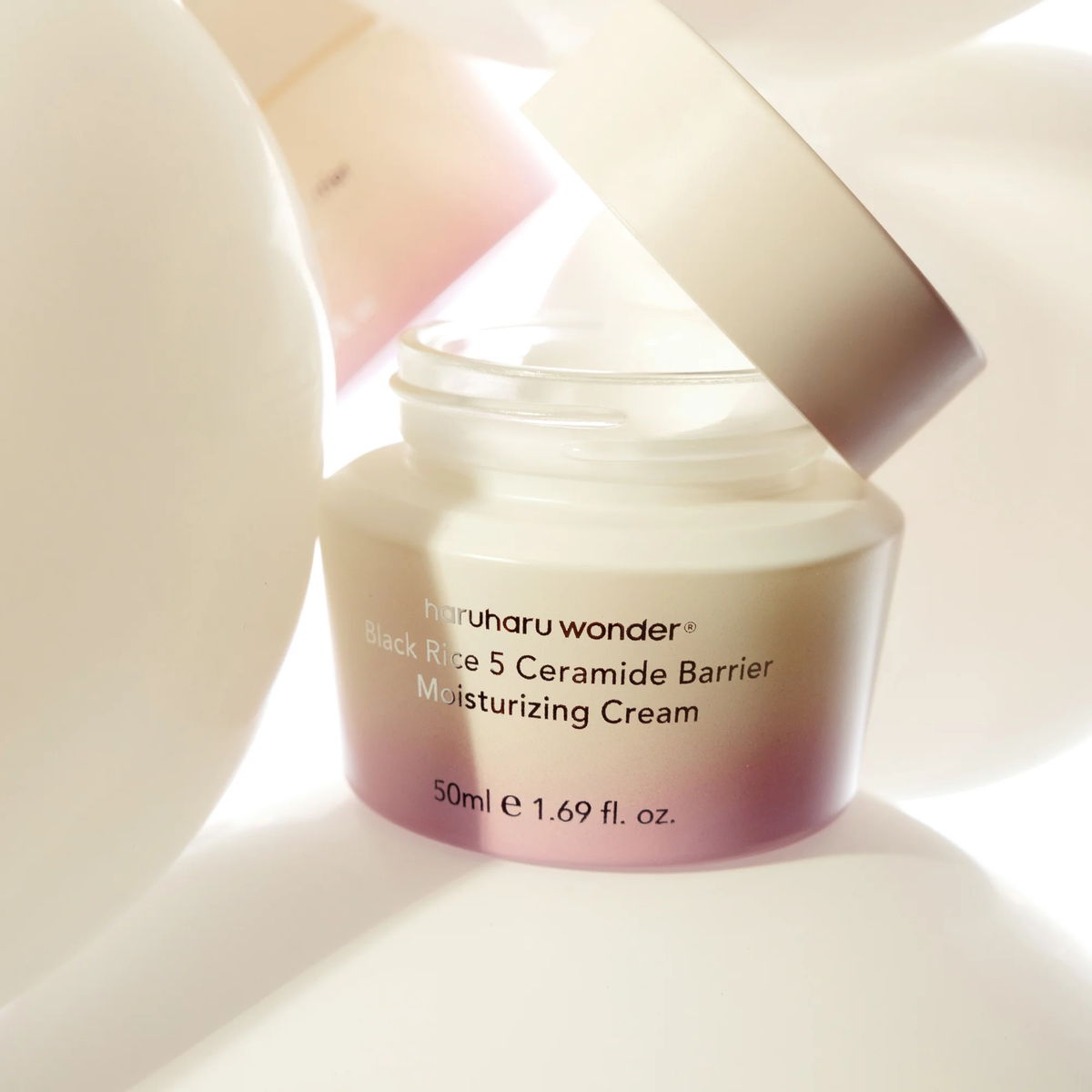 Pot ouvert de crème entouré de formes arrondies claires