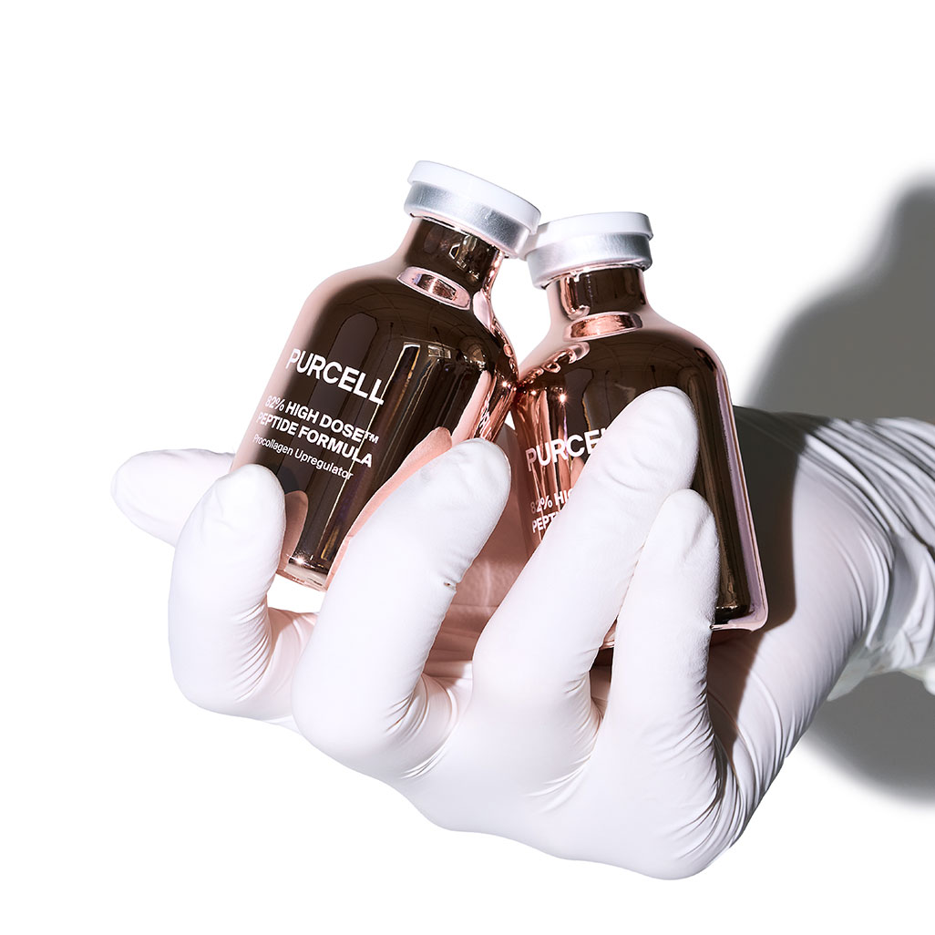Deux flacons de sérum rose métallisé tenus par des mains gantées
