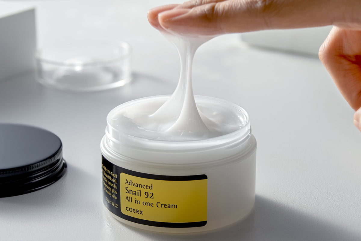 Texture filante de crème blanche étirée entre le doigt et le pot