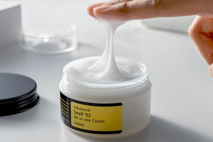 Texture filante de crème blanche étirée entre le doigt et le pot