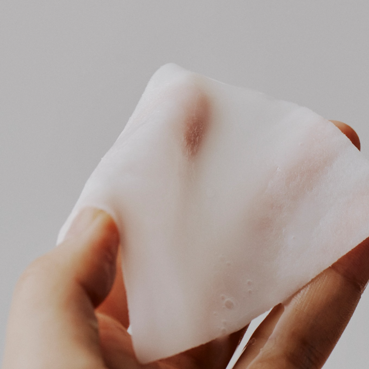 Disque de soin fin et blanc étiré entre les doigts