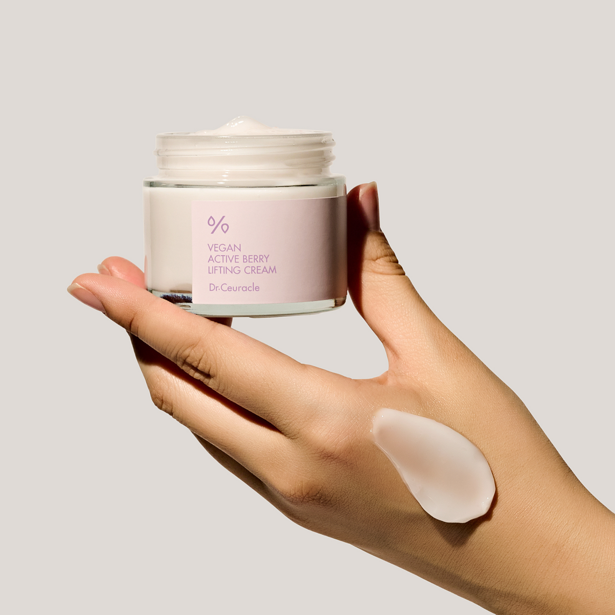 Pot ouvert tenu dans la main avec une trace de crème sur le dos de la main