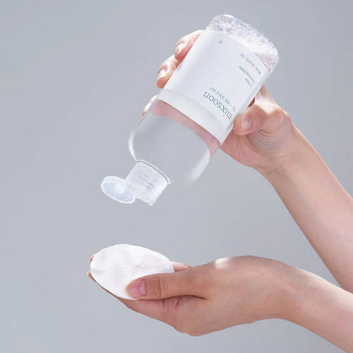 Eau nettoyante versée sur un coton tenu en main