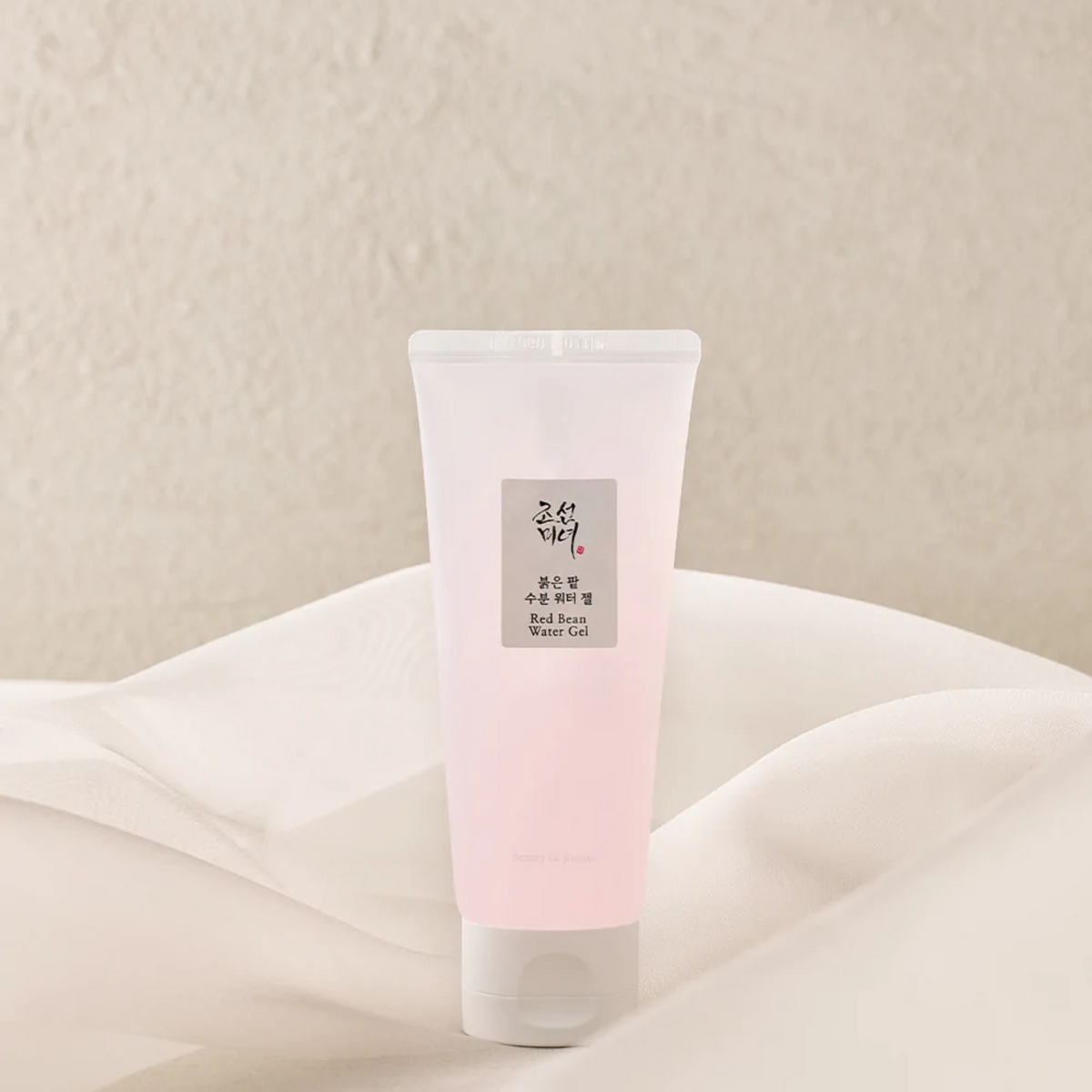 Tube rose pâle de gel hydratant posé sur un tissu clair