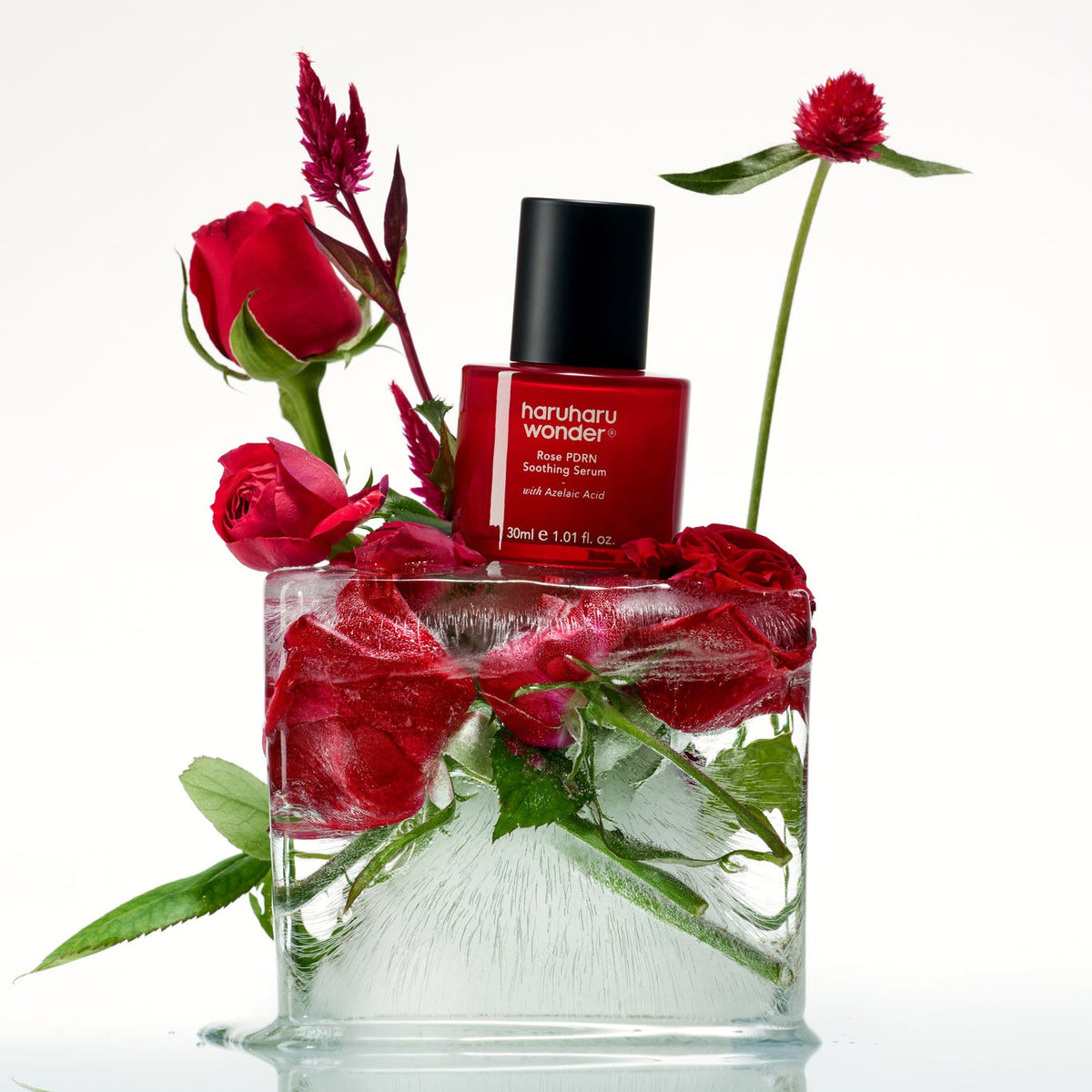 Flacon rouge de sérum posé sur de la glace contenant des roses