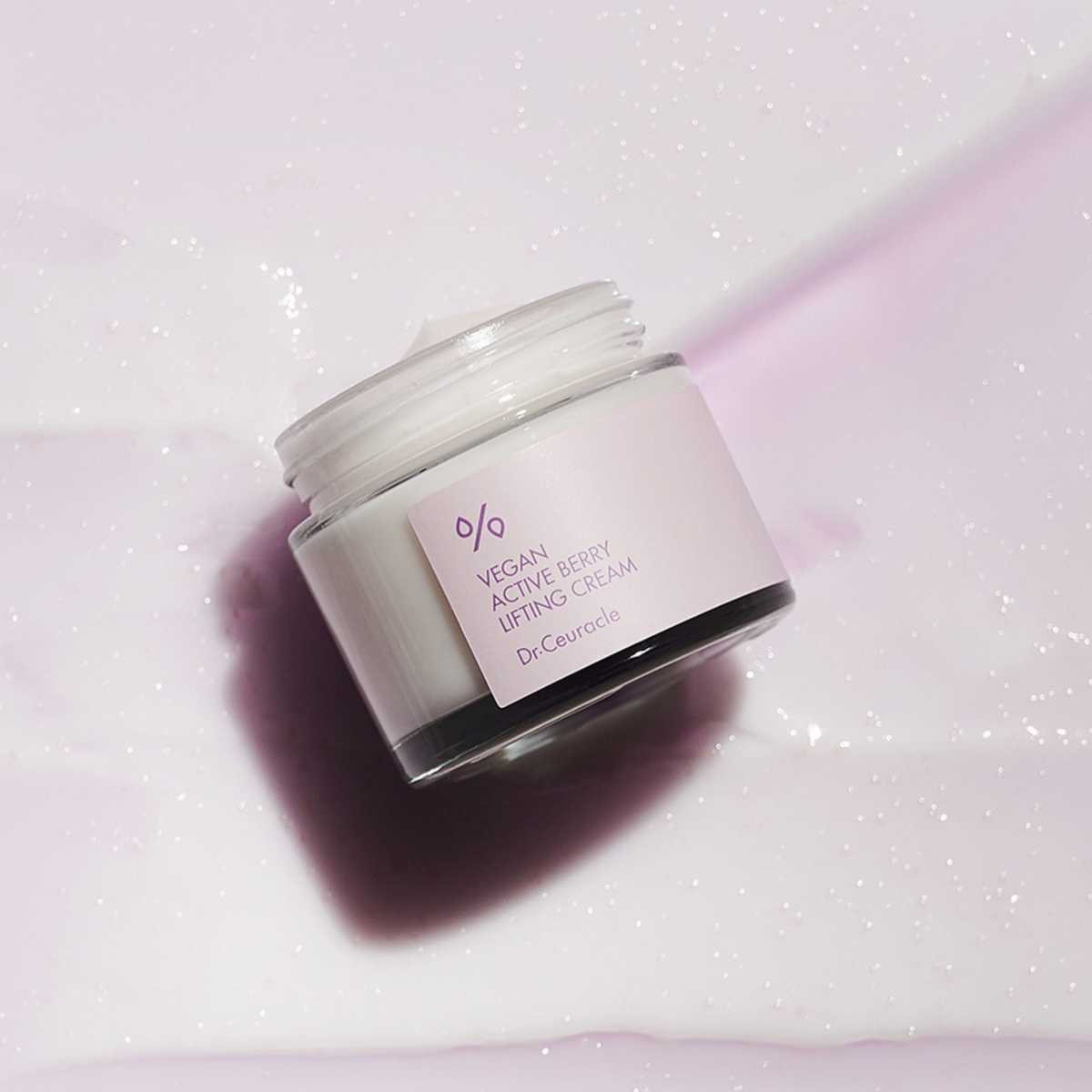 Pot de crème ouvert posé sur un tissu mauve