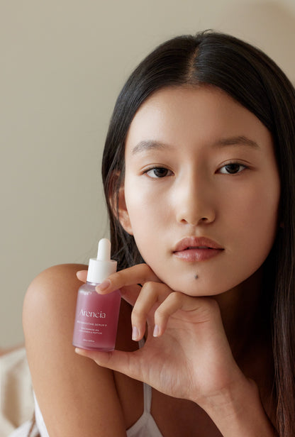 Flacon de sérum rose tenu près du visage