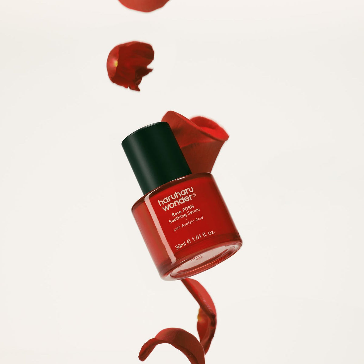 Flacon rouge de sérum entouré de pétales de rose