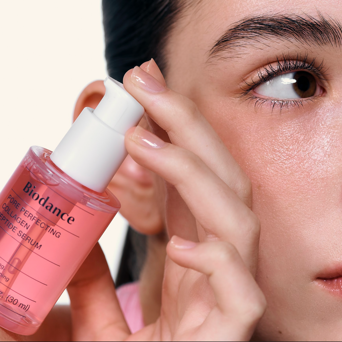 Flacon-pompe de sérum rose tenu près de la joue