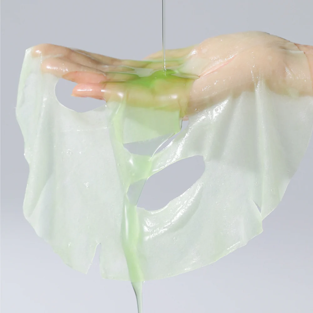 Masque en tissu imbibé de soin vert clair déplié sur la main